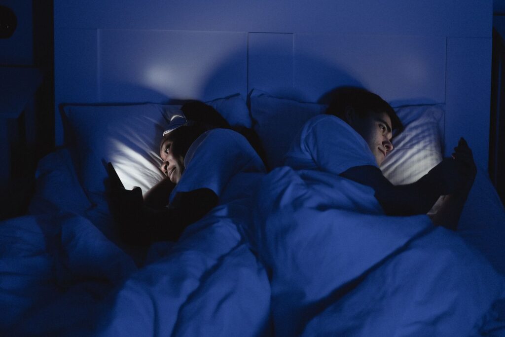 Couple lying back to back in bed, each on a phone, a picture of digital dependence